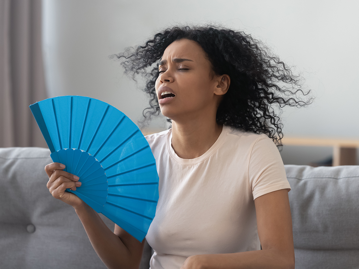 Woman cooling herself with a handheld fan because her AC doesn’t work well.