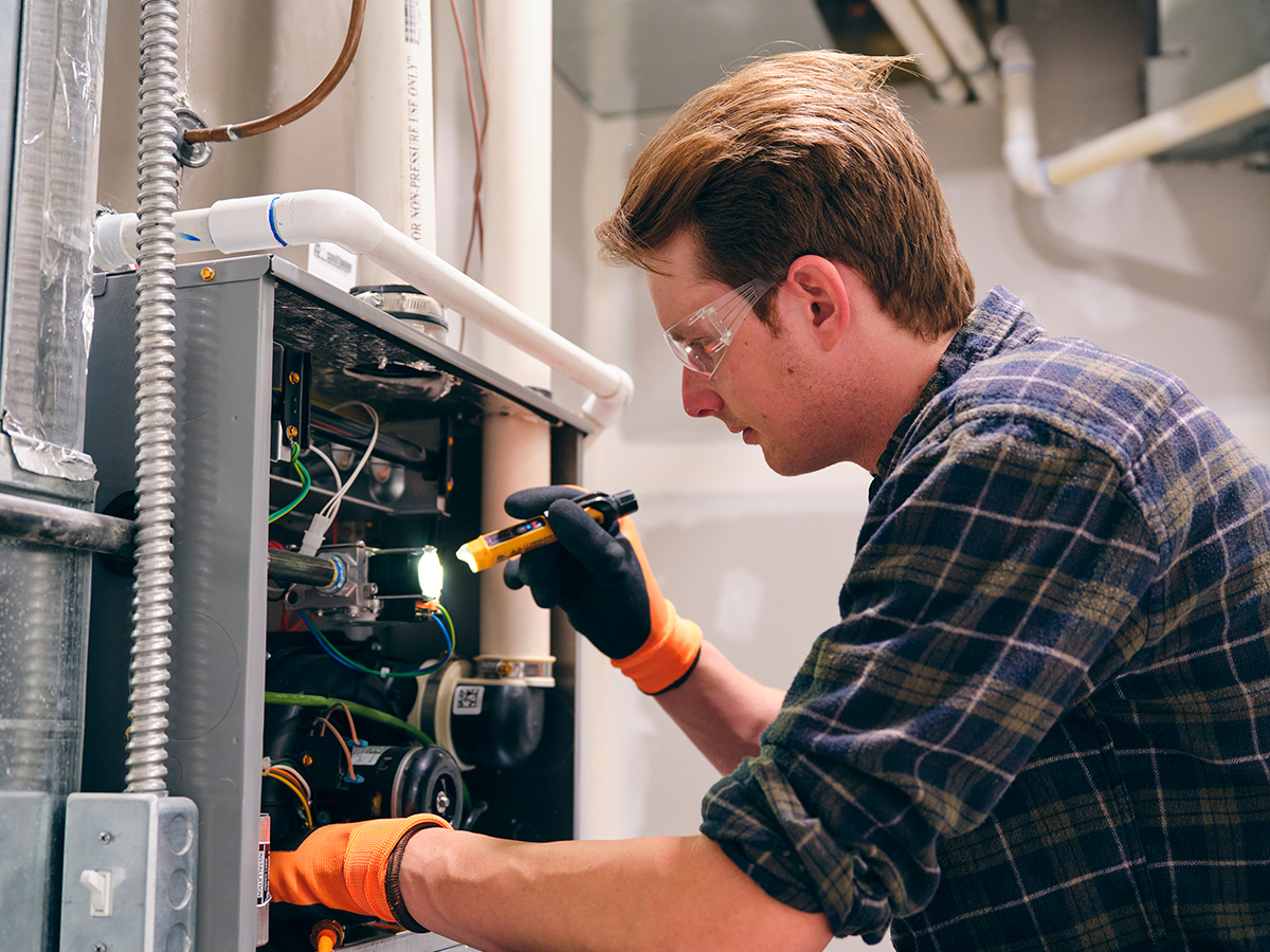 HVAC technician using a flashlight to examine the back panel of a unit.