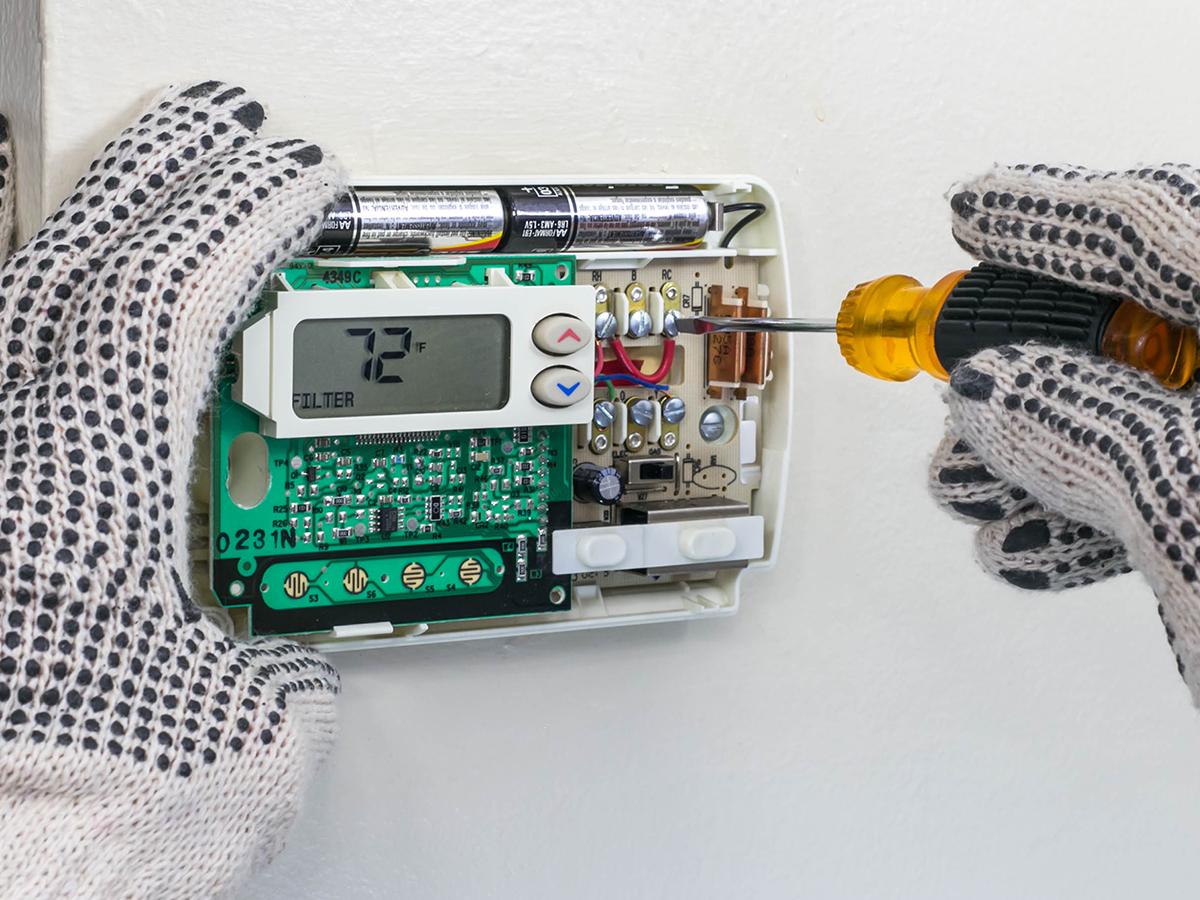 Someone working on a thermostat that they took apart.