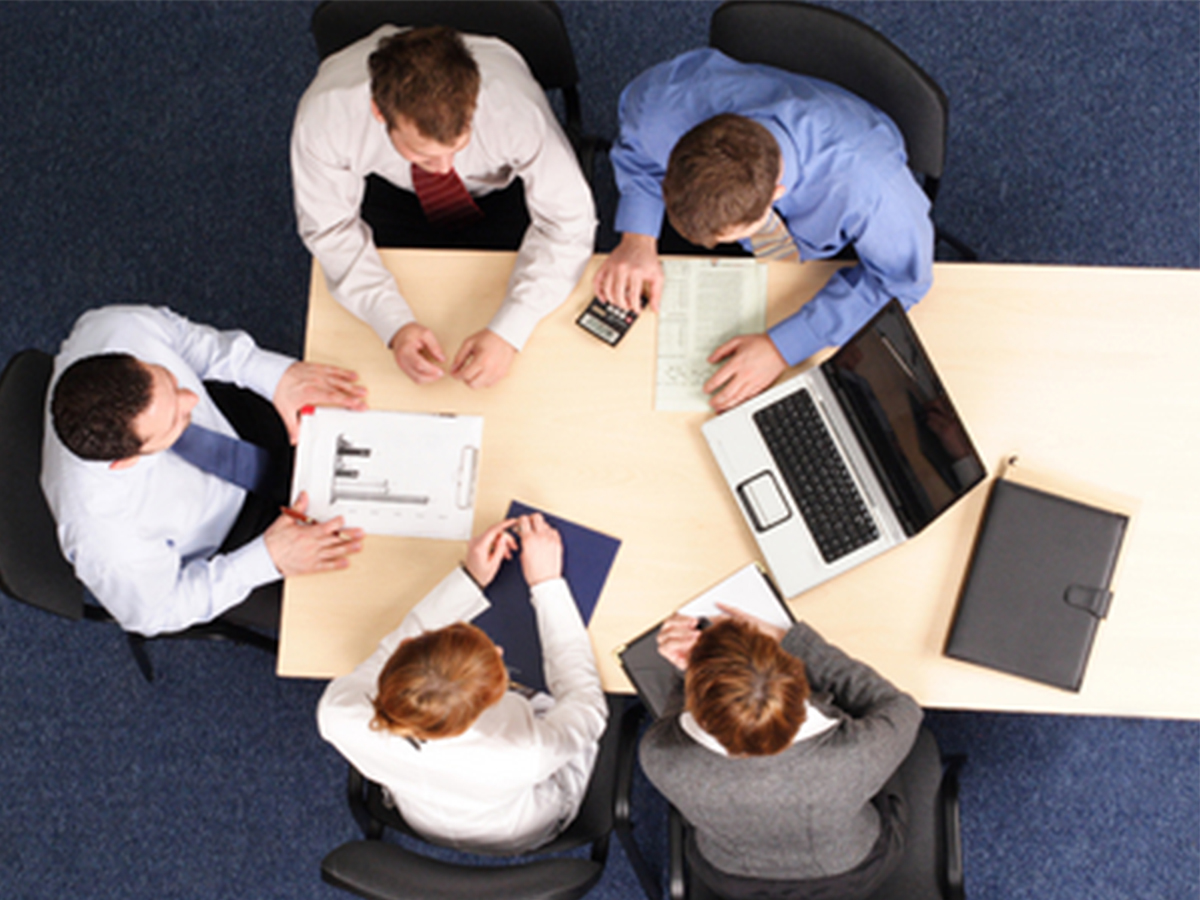 OVerhead view of five employees in business attire sitting at a table working together.